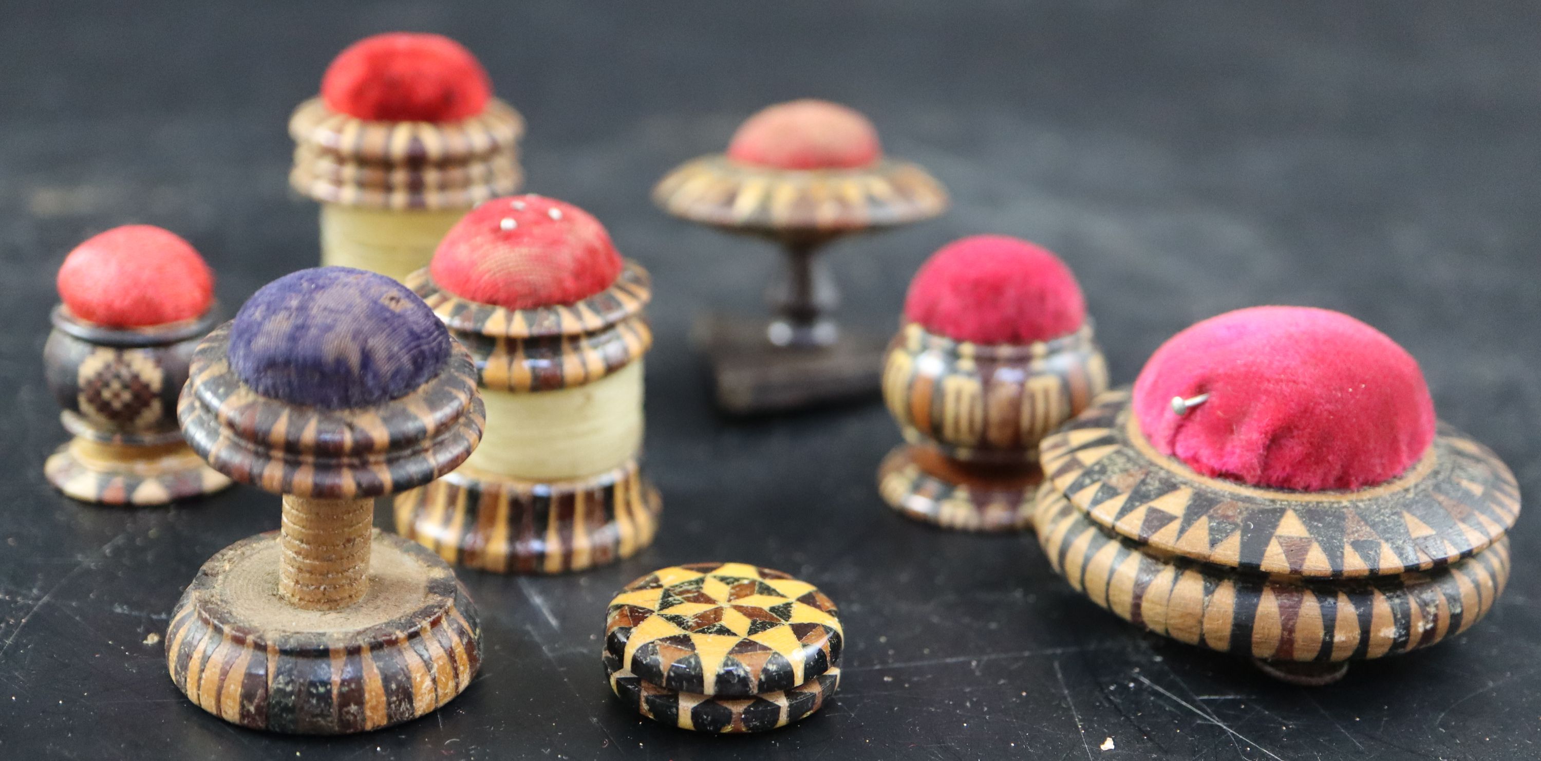 Seven assorted Victorian Tunbridgeware pin cushions and a small spool
